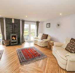 A living room with two cream leather sofas a fireplace rugs and glass doors leading outside at Nant Y Felin Lodge in Aberdaron