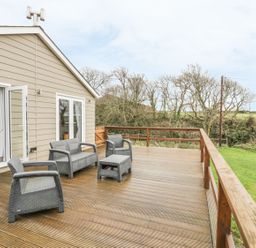 An outdoor wooden deck with gray patio furniture and a view of trees and grass at Nant Y Felin Lodge in Aberdaron