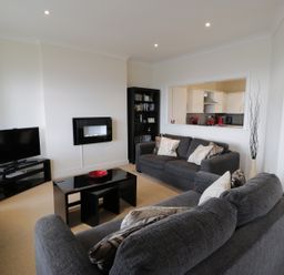 A living room with grey sofas a black coffee table a tv and a doorway to a kitchen at Apartment 3 Marian Y Mor in Pwllheli