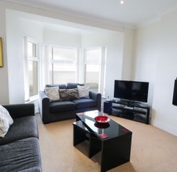 A living room with two gray sofas a black coffee table with a red bowl a television and a view of the sea through large windows at Apartment 3 Marian Y Mor in Pwllheli