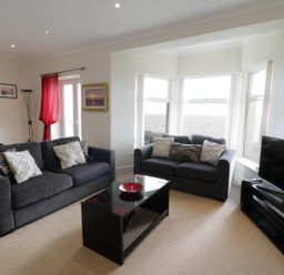 A living room with two grey sofas and a black coffee table facing a television by bay windows at Apartment 3 Marian Y Mor in Pwllheli
