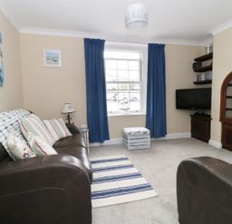 A living room with brown leather sofas blue curtains a striped rug a television and a wooden cabinet at No 9 Watchet