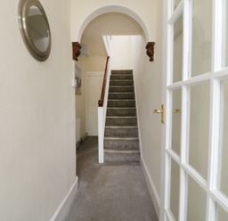 A hallway with carpeted stairs a white door a round wall mirror and a glass panel door at No 9 in Watchet