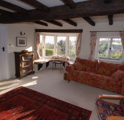 A living room with exposed wooden beams a red patterned sofa and a large window with a curved bench at Appletree Cottage in Higher Brimley near Bovey Tracey