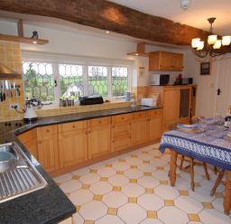 A kitchen with wooden cabinets a dining table set with plates and glasses and a window with a countryside view at Appletree Cottage in Higher Brimley near Bovey Tracey
