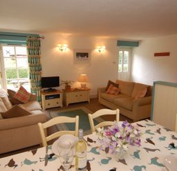 A living room with two beige sofas a small television and a dining table with flowers at The Coach House in Ugborough