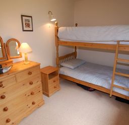 A bedroom with bunk beds a wooden dresser with a lamp and mirror at The Coach House in Ugborough
