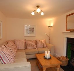 A living room with a beige sofa striped cushions wooden coffee table candles fireplace and framed pictures at Jordan House Boscastle