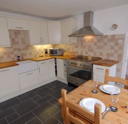 A kitchen with white cabinets wooden countertops a dining table set with plates glasses and a vase with flowers at Jordan House in Boscastle
