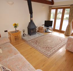 A living room with two sofas a stove a television on a stand and a rug on wooden floor at The Milking Parlour in Wookey