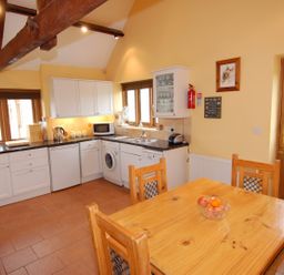 A kitchen with white cabinets wooden dining table and chairs and a door at The Milking Parlour in Wookey