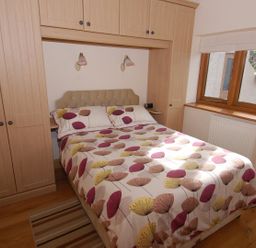 A bedroom with a double bed and built-in wooden wardrobes near a window at The Milking Parlour in Wookey