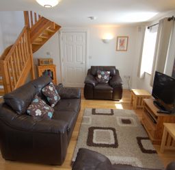 A living room with leather sofas a patterned rug wooden stairs and a television at The Old Cider Barn in Wookey