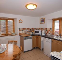 A kitchen with wooden table and chairs dishwasher microwave and sink with windows at The Old Cider Barn in Wookey