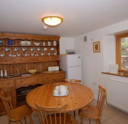 A kitchen with wooden cabinets and dining table with chairs and a refrigerator by the window at The Old Cider Barn in Wookey
