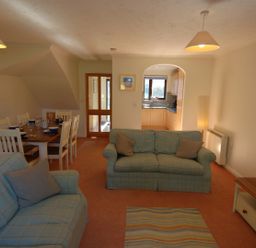 A living room with two sofas and a dining table set with dishes with a view into the kitchen at Pine Cottage in Maenporth