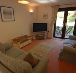 A living room with two sofas a coffee table a television and glass doors leading to a patio at Pine Cottage in Maenporth