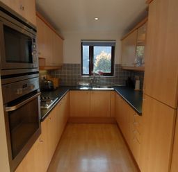 A kitchen with wooden cabinets a double oven a sink below a window and a tiled backsplash at Pine Cottage in Maenporth