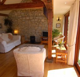 A living room with wooden beams stone wall white sofas and large windows at Sunnyside in Staple Fitzpaine