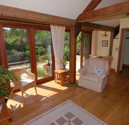 A living room with wooden beams glass doors and armchairs at Sunnyside in Staple Fitzpaine