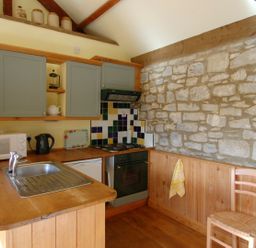 A kitchen with wooden countertops cabinets a stone wall and a wooden chair at Sunnyside in Staple Fitzpaine