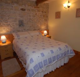 A bedroom with a double bed two bedside tables with lamps wooden flooring and stone and painted walls at Sunnyside in Staple Fitzpaine