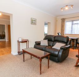 A living room with a black leather sofa, wooden coffee table, side table, and rocking chair at Little Waycroft in Dawlish