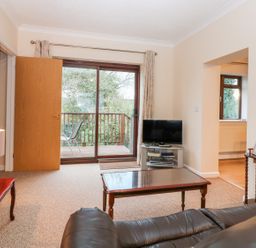 A living room with a leather sofa coffee table television and sliding glass door leading to balcony at Little Waycroft in Dawlish