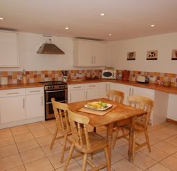 A kitchen with wooden table and chairs a stove microwave and tiled backsplash at West Perry Hay in North Chideock near Chideock