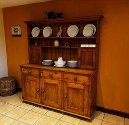 A wooden dresser with plates and bowls on shelves in a room with orange and beige walls at West Perry Hay in North Chideock near Chideock