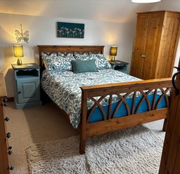 A bedroom with a wooden bed and blue patterned bedding blue bedside tables with lamps a wooden wardrobe and dresser at West Perry Hay in North Chideock near Chideock