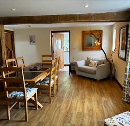 A dining area with a wooden table and chairs next to a small gray couch and windows at West Perry Hay in North Chideock near Chideock