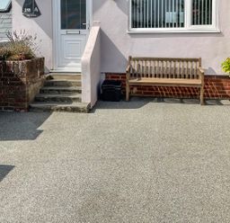 The front entrance of a house with concrete steps a wooden bench a window a planter with plants and a door at Monkbarns in Brixham
