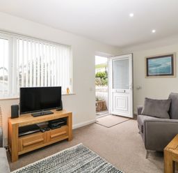 A living room with a television on a wooden stand a gray armchair and an open door at Monkbarns in Brixham