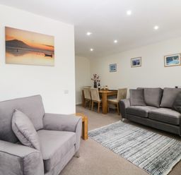 A living room with two gray sofas a patterned rug a wooden dining table with chairs and landscape pictures on the walls at Monkbarns in Brixham