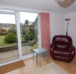 A room with a leather armchair glass tables and a door opening to a garden at Garden View in Kingskerswell