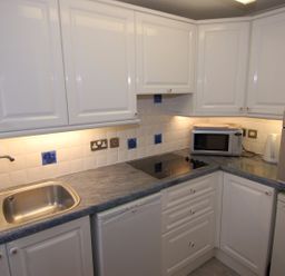 A kitchen with a sink, white cabinets, a microwave, an oven, and a stove at Garden View in Kingskerswell