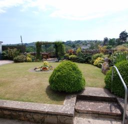 A garden with a lawn a flower bed shrubs stone steps and a wooden pergola at Garden View in Kingskerswell