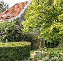 A stone house with a red tiled roof surrounded by trees and shrubs at The Granary Edington near Street and Glastonbury