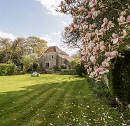 A garden with a lawn table and chairs near a stone house and blossoming tree branches at The Granary in Edington near Street and Glastonbury