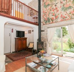 A living room with a glass coffee table flowers on the table wooden cabinet television wood burner and stairs to a mezzanine at The Granary in Edington near Street and Glastonbury