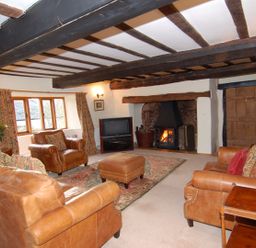A living room with leather sofas and armchairs a television and a fireplace at Surridge Farmhouse in Waterrow