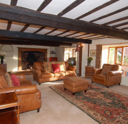 A living room with leather sofas a patterned rug wooden beams on the ceiling and a fireplace at Surridge Farmhouse in Waterrow