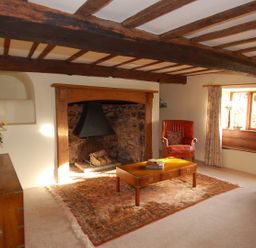 A living room with wooden beams a stone fireplace a wooden coffee table and armchairs at Surridge Farmhouse in Waterrow