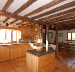A kitchen with wooden cabinets a countertop island and a dining table in the background at Surridge Farmhouse in Waterrow