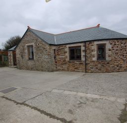 A single story stone house with multiple windows and a gray roof on a concrete driveway at Hideaway in Tintagel