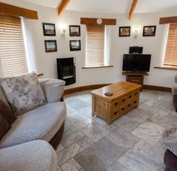 A seating area with sofas a wooden coffee table a television and windows with blinds at Hideaway in Tintagel