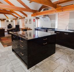 An open plan kitchen and living area with wooden ceiling beams a black kitchen island dining table and chairs and a television at Hideaway in Tintagel