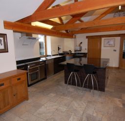 A kitchen with wooden beams tiled floor black countertop island with two stools wooden cabinets and framed pictures at Hideaway in Tintagel