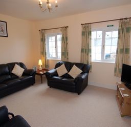 A living room with black leather sofas a wooden TV stand with a television and windows with curtains at The Barn in Tregoodwell